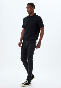 Camisa polo negra de mangas cortas, con tejido texturizado, combinada con jeans negros de corte slim y zapatillas negras con suelas blancas.