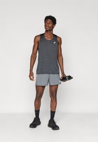 Αθλητικό τοπ σε σκούρο γκρι χρώμα με λογότυπο στο πλάι, συνδυασμένο με ανοιχτό γκρι σορτς. Η φιγούρα κρατάει ένα μαύρο μπουκάλι νερού και φοράει μαύρα αθλητικά παπούτσια.