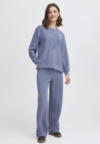 Sweat-shirt bleu clair et pantalon large assorti en tissu doux. Le sweat-shirt présente un motif abstrait bleu foncé sur le devant.