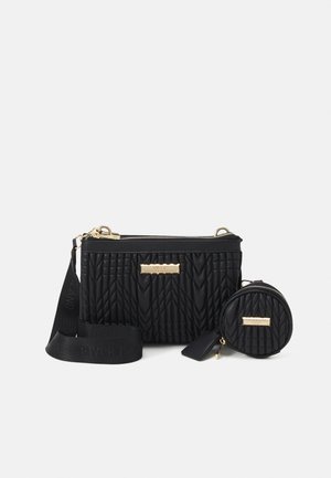 Bolso bandolera negro acolchado con cremallera dorada y placa con logotipo, cuenta con una correa ajustable y un pequeño monedero redondo adjunto.