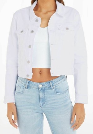 Frau trägt eine weiße, kurze Jeansjacke über einem weißen, gerippten Crop-Top und hellblauen, hoch taillierten Jeans.