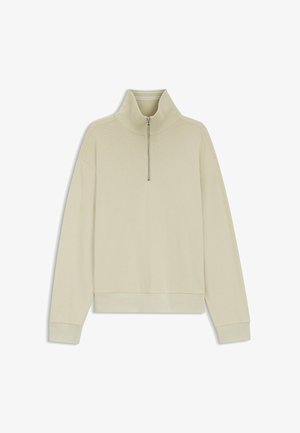 Vaaleanbeige pitkähihainen pusero, jossa on ribbineulos, korkea kaulus ja hopeanvärinen neljänneksen vetoketjusuljenta edessä.