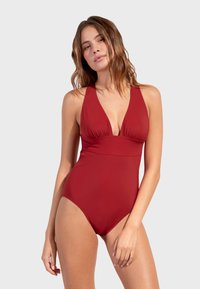 Traje de baño rojo de una sola pieza con escote en V profundo, bodice fruncido y piernas de corte alto. Hecho de un tejido suave y elástico, que ofrece una silueta ajustada.