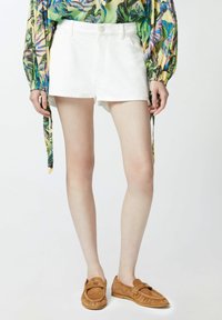 Bijele traper kratke hlače s visokim strukom i klasičnim dizajnom s pet džepova, uparene s bež antilop klompfama.