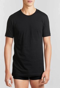 T-shirt in cotone nero, maniche corte, collo rotondo, tessuto morbido, vestibilità dritta, indossata con pantaloni corti neri, tessuto liscio su uno sfondo neutro.