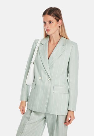 Hellgrüner, doppelt geknöpfter Blazer mit weißen Nadelstreifen, breiten Revers und zwei aufgesetzten Taschen, kombiniert mit einer weißen Schultertasche.