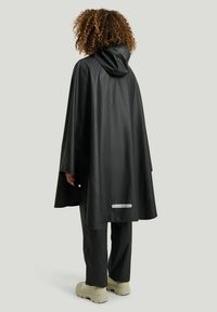 Svart vattentät poncho med huva, med lös passform och reflexdetalj vid fållen. Slät textur och hållbart material.