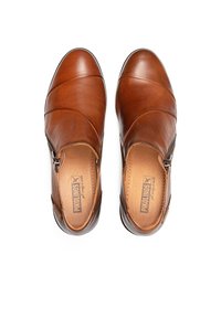 Chaussures en cuir marron à enfiler avec des coutures diagonales, dotées d'une fermeture éclair sur le côté et d'une texture lisse. L'intérieur est beige avec une marque.
