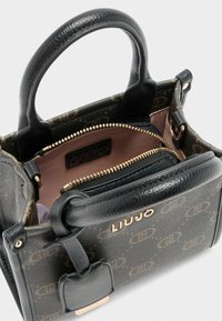 Zwarte leren handtas met gouden hardware en een gemusterde buitenkant. Geopend, onthullend een roze interieur en logo label binnenin.
