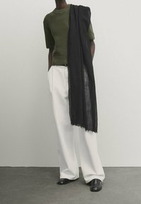 Olivengrøn ribstrikket kortærmet sweater, hvide vidbenede bukser, sort let tørklæde med frynser og sorte slip-on sko.