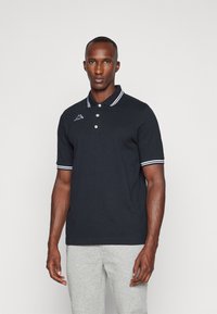 Polo shirt blu navy con strisce bianche col collo e maniche. Presenta tre bottoni e un logo ricamato sul petto. Materiale in cotone.