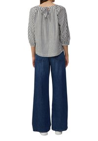 Zwart-wit gestreepte blouse met driekwartmouwen en een strikdetail aan de achterkant. Gelijkend met wijde blauwe denimmer jeans.