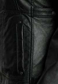 Zwart leren jack met een gestructureerd oppervlak, gedetailleerde stiksels en een rechthoekige zak met een drukknoopsluiting.