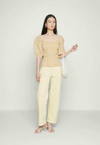 Top amarelo xadrez com mangas bufantes e decote quadrado, combinado com calças largas em tom crème. Acessório com uma mala branca texturizada.