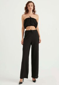 Black cropped strapless top with ruched texture, paired with high-waisted, wide-leg black pants in a vertical striped pattern.