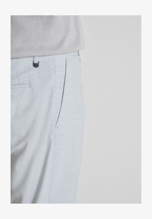 Svijetlosive teksturirane hlače za odijelo nošene s uvučenom bež košuljom, fokus na struk i dio s džepom na jednostavnoj pozadini.