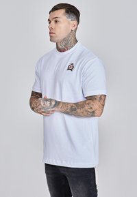 Bijela majica kratkih rukava od pamuka s okruglim izrezom, s vezenim logotipom na prsima i ravnim rubom.