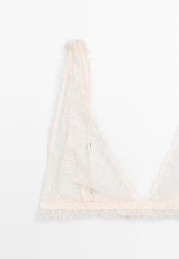 Lace bralette in pale pink with a soft, textured design, featuring frayed edges and delicate floral patterns along the straps and hem.
