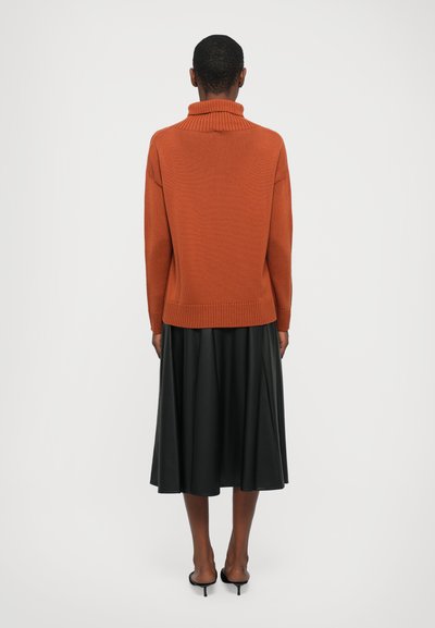 Rust-colored knit turtleneck sweater with ribbed hem, paired with a black, flowing, below-the-knee leather skirt and black heeled sandals.