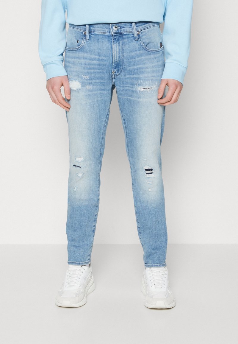 Ljusblå denimjeans med slim fit, med slitna detaljer, blekning och traditionell femfickorsdesign. Matchad med vita sneakers.