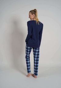 Camiseta de manga larga en navy combinada con pantalones de pijama de cuadros en azul y blanco. Tejido suave con un corte relajado. Los pantalones cuentan con bolsillos laterales.