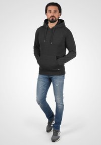 Dark grey hoodie with a front pocket, adjustable drawstrings, and ribbed cuffs, paired with distressed blue jeans and grey sneakers.