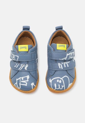 Niebieskie buty dla małych dzieci z białymi abstrakcyjnymi wzorami, podwójnymi paskami na rzepy, żółtymi metkami z logo Camper i brązowymi podeszwami, widoczne z góry.