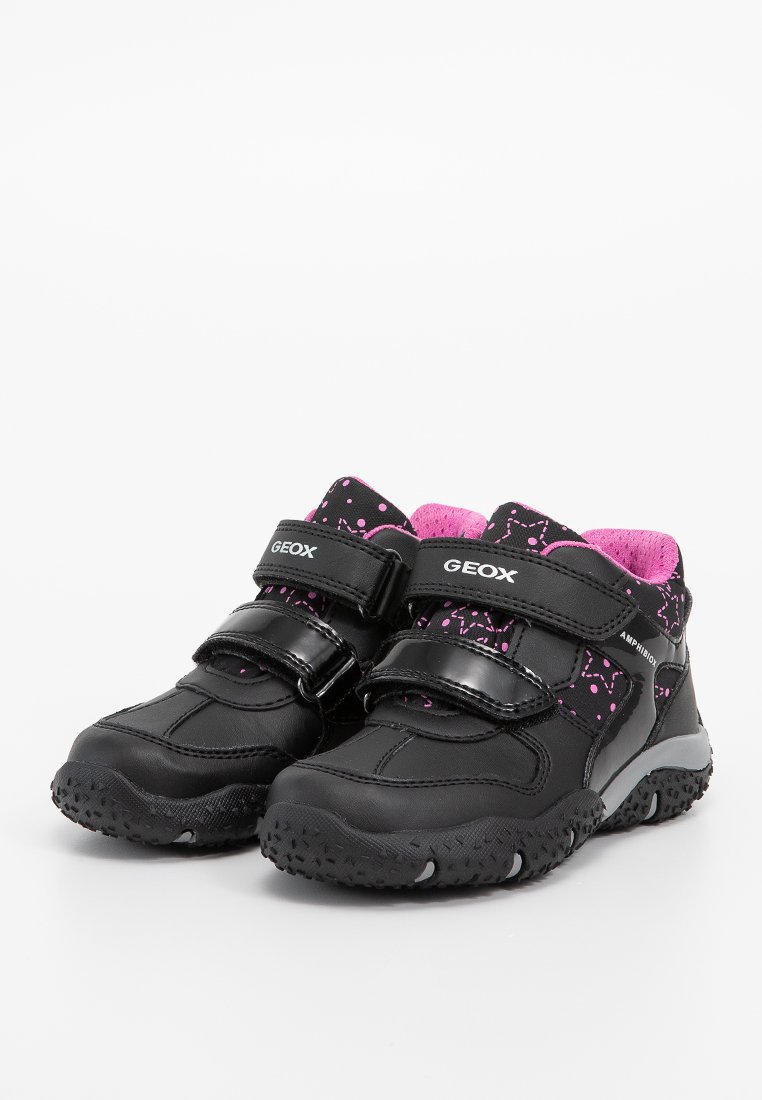 Schwarze Kinderschuhe mit pinken Akzenten, Klettverschlüssen, einer strukturierten Gummisohle und einem gemusterten Innenfutter mit kleinen pinken Punkten.