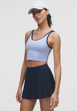 Top sportiv scurt, ajustat, de culoare albastru deschis, cu margini de un albastru închis, asortat cu o fustă plisată de culoare albastru închis. Materialul pare elastic și neted.