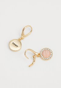 Gullfargede øredobber med et sirkulært design. Den ene siden har en rosa stein omgitt av klare rhinesten, mens den andre har DKNY-logoen.