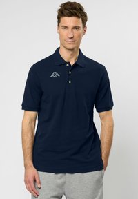 Navyblauwe poloshirt van katoen met korte mouwen, drie-knopenknopsluiting en een wit logo op de linkerkant van de borst.
