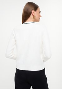 Suéter blanco de punto con mangas largas y una silueta ajustada. Presenta puños y dobladillo acanalados, con un acento negro en el cuello.