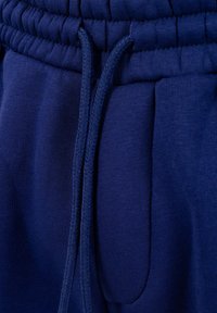 Primer plano de pantalones deportivos azul marino con cintura elástica y cordón atado en un nudo simple.