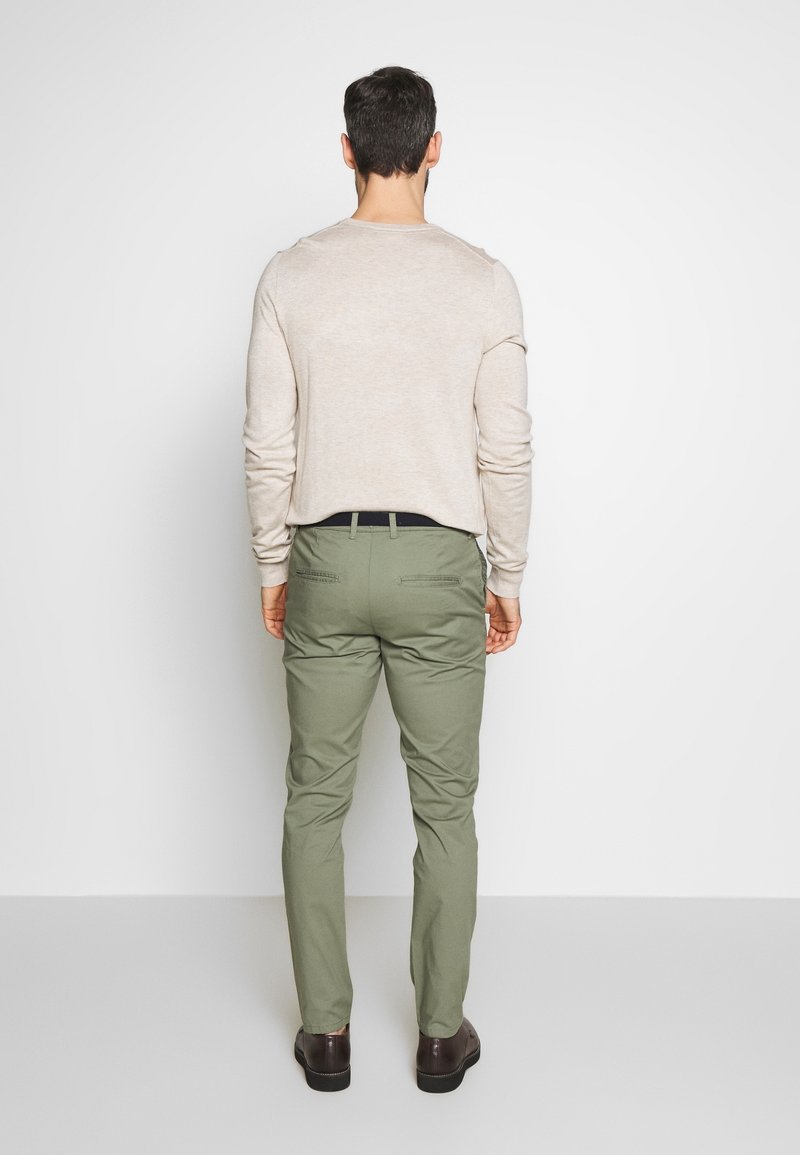 Beige långärmad skjorta, olivgrön skräddarsydd byxa och mörkbruna skor. Outfiten har en avslappnad passform med minimal detaljering.