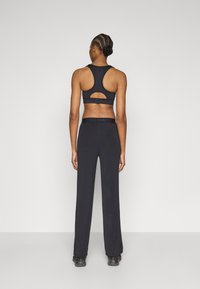 Čierna športová podprsenka s vykrojeným detailom na chrbte, doplnená voľnými čiernymi nohavicami. Hladká látka s priliehavým pásom a minimálnym označením značky.