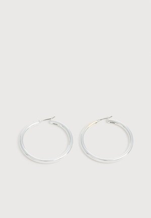 Paire de boucles d'oreilles créoles argentées brillantes avec fermoirs en fil fin, présentée sur un fond gris clair.