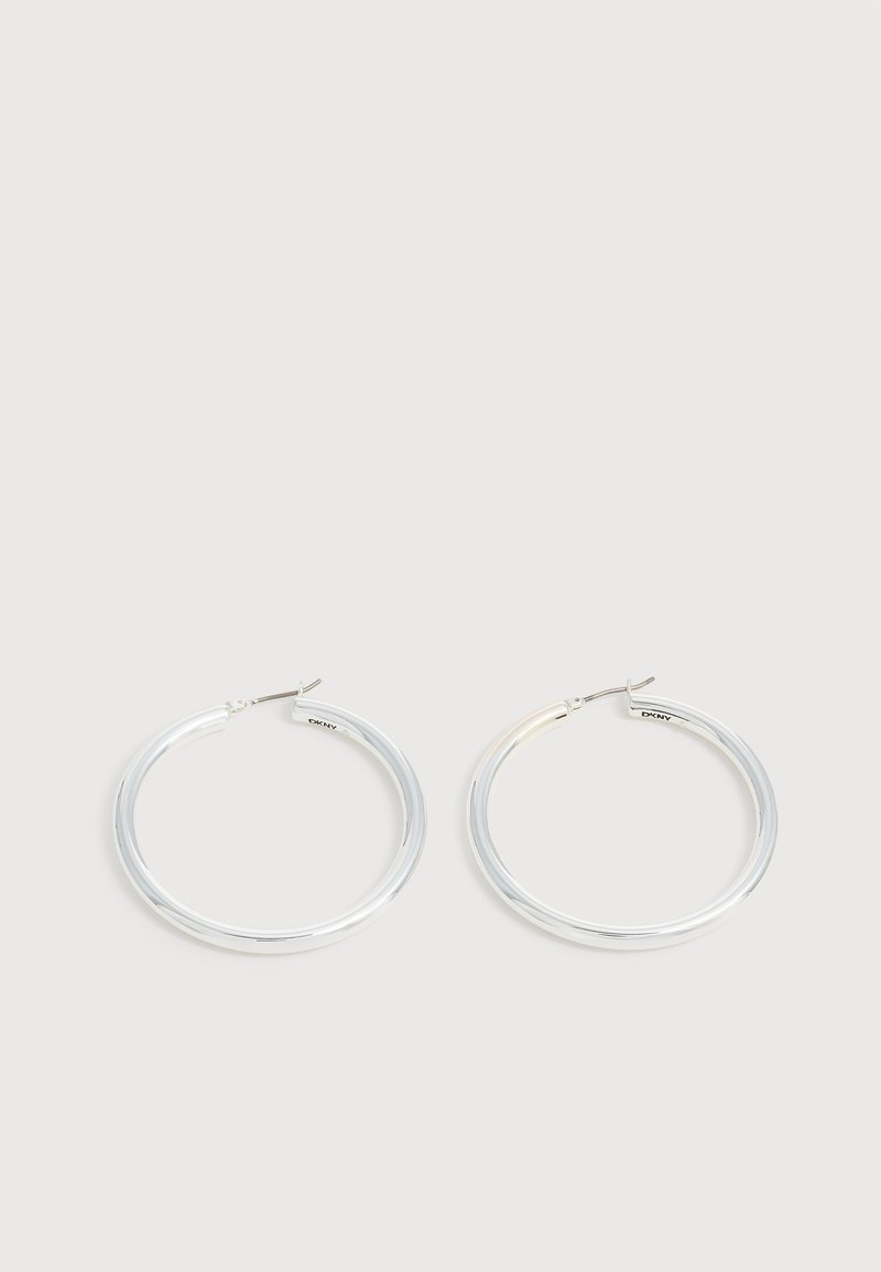 Paire de boucles d'oreilles créoles argentées brillantes avec fermoirs en fil fin, présentée sur un fond gris clair.