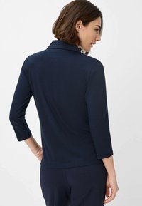 Marineblå langærmet top med krave og 3/4-lange ærmer. Blødt stof med en glat overflade, der har en subtil detalje med bagsømsseam.