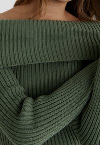Zelený žebrovaný pletený svetr s designem odhalených ramen. Obsahuje strukturovaný materiál a široké žebrování pro moderní vzhled.