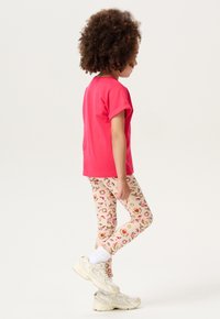 Un t-shirt rose à manches courtes associé à un legging crème avec des motifs floraux. Des baskets blanches et grises complètent la tenue.