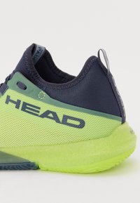 Baskets avec une tige en mesh bleu marine et vert lime, présentant une semelle texturée et un logo "HEAD" bien visible sur le côté.