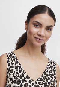 Mouwloze jurk met luipaardprint en een diepe V-halslijn, gemaakt van gladde stof. Heeft zwarte en bruine vlekken op een beige achtergrond.