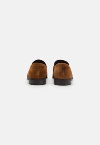 Loafers din suede maro cu vârf rotund, talpă din cauciuc negru și branding subtil pe călcâi, având o textură netedă și un design minimalist.