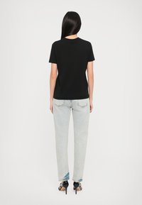 Black cotton t-shirt, short sleeves, round neck, paired with light blue high-waisted jeans, and black high-heeled sandals with a shiny finish.