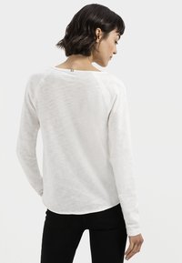 Witte lange mouwen top met een ontspannen pasvorm, gekenmerkt door een afgeronde zoom en raglanmouwen; vervaardigd uit lichtgewicht, licht gestructureerde stof.