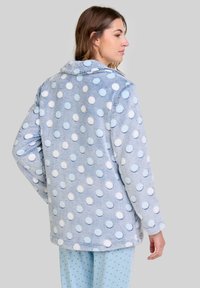Chaqueta de forro polar azul claro con grandes lunares blancos y azul claro, que cuenta con un cuello y dos bolsillos laterales. Tejido suave y texturizado.