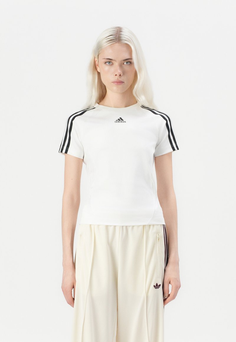 Weißes Kurzarm-Sportshirt mit schwarzen drei Streifen an den Schultern und kleinem schwarzen Logo auf der Brust. Glattes, eng anliegendes Design, Rundhalsausschnitt.