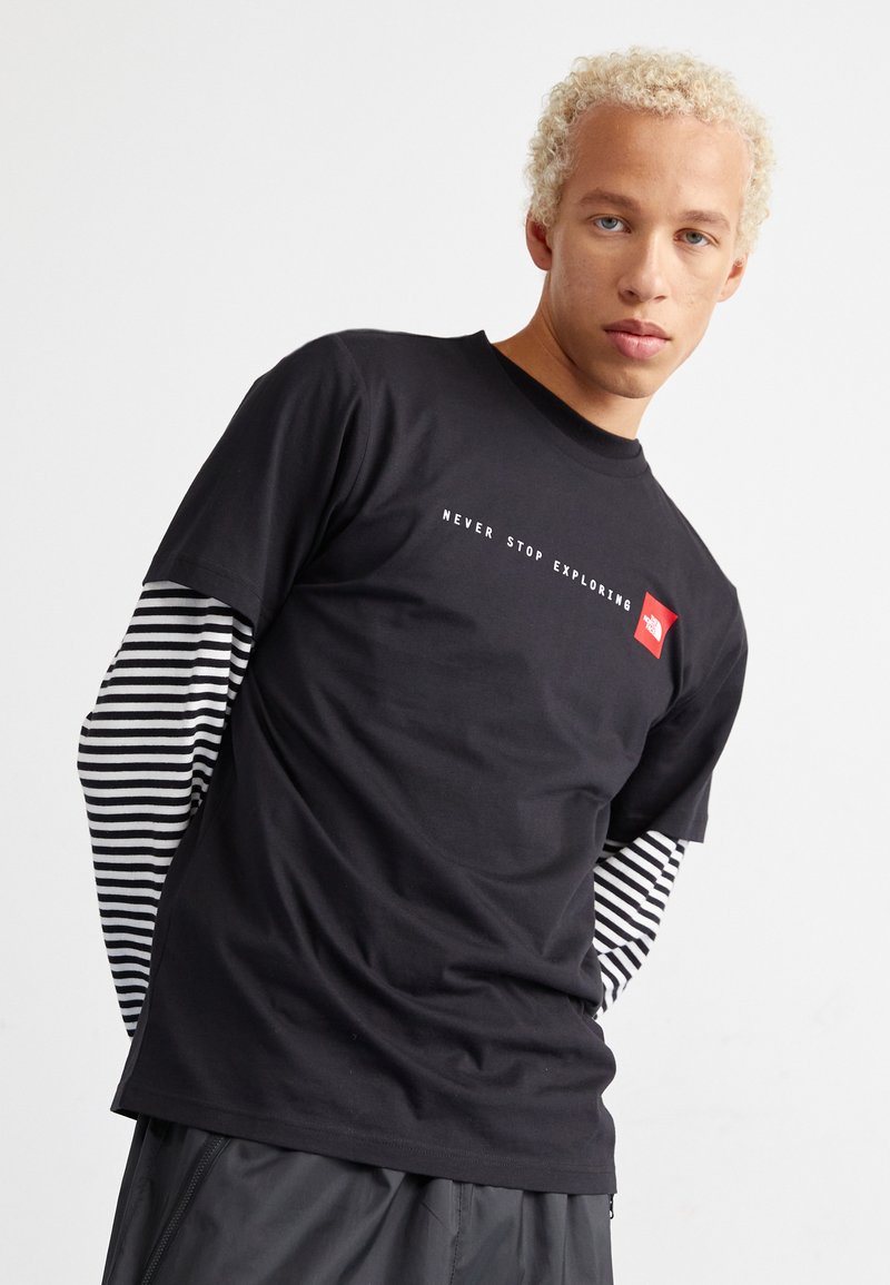 Zwarte katoenen t-shirt met de tekst "NEVER STOP EXPLORING"; gelaagd met een gestreepte lange mouwen shirt eronder. Korte mouwen en een ronde hals ontwerp.