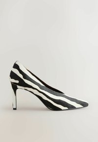 Chaussure à talon haut à rayures zébrées noir et blanc, avec bout pointu et talon stiletto fin, vue de profil gauche sur fond neutre.