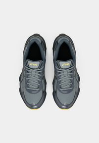 Γκρι αθλητικά παπούτσια με πλέγμα και συνθετικά υλικά, με στρογγυλή μύτη, υφασμάτινες πάνελ και κίτρινες λεπτομέρειες στο λογότυπο και στη σόλα.